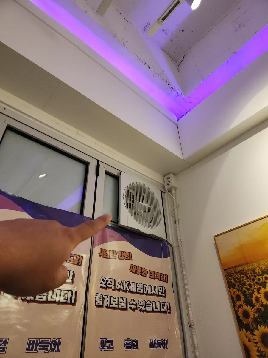 벽 상단 모서리 근처에 설치된 환풍기 위치를 손으로 가리키는 장면