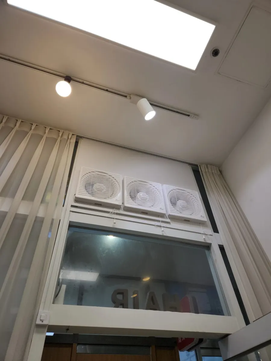 높은 창 상단에 흰색 환풍기 세 대가 나란히 설치된 매장 내부