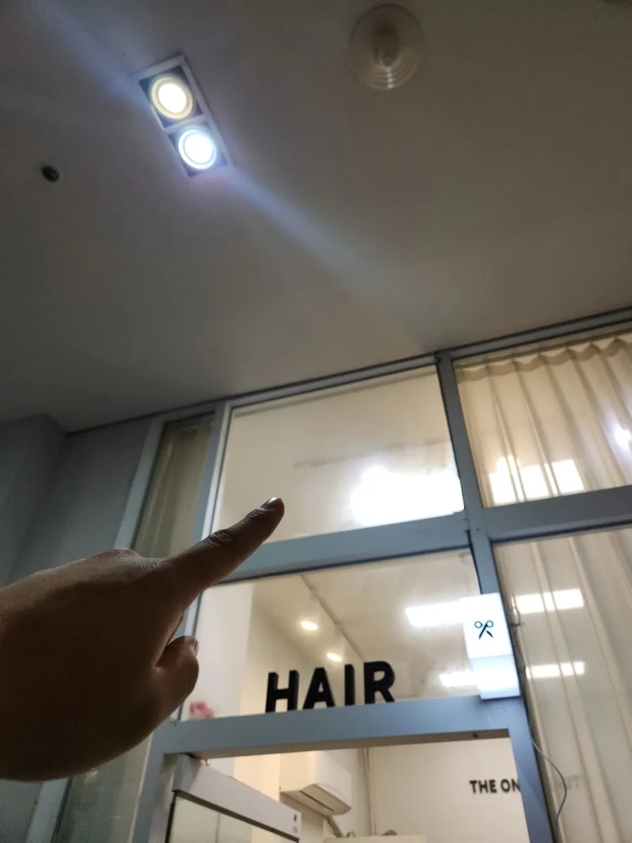 유리 출입문 위 천장 조명이 보이는 미용 매장 입구