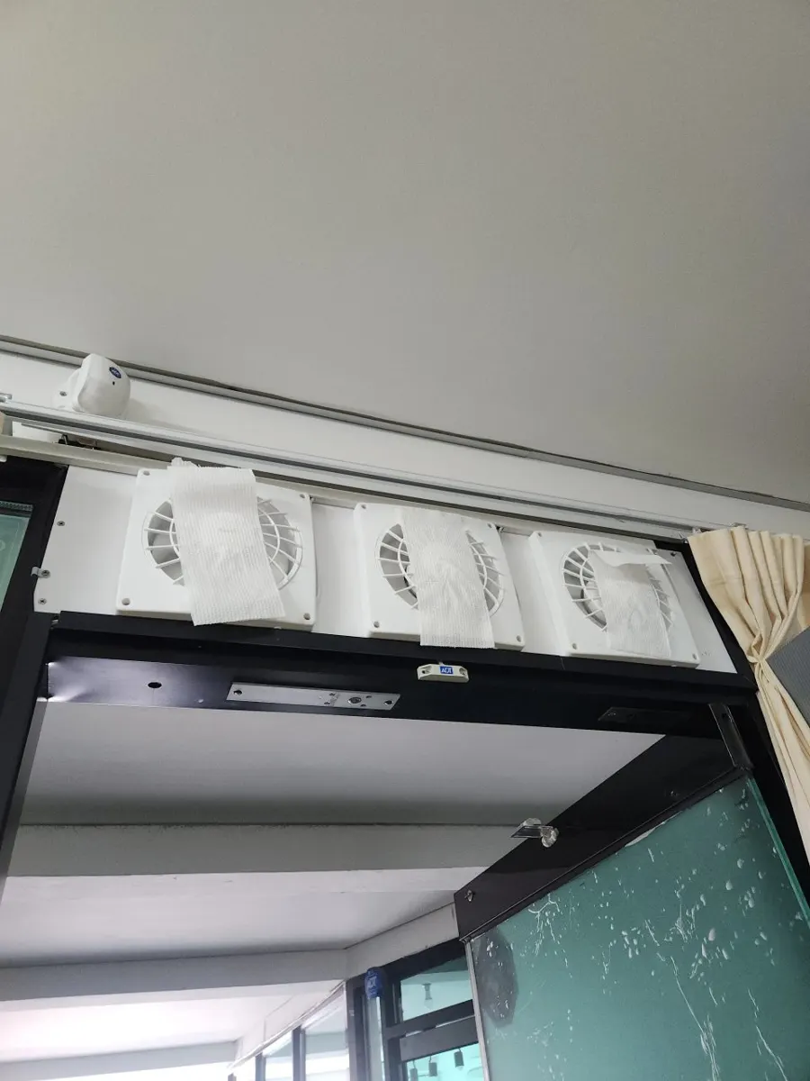 문틀 상단에 설치된 흰색 환풍기 세 대에 휴지를 대어 흡입력을 확인하는 장면