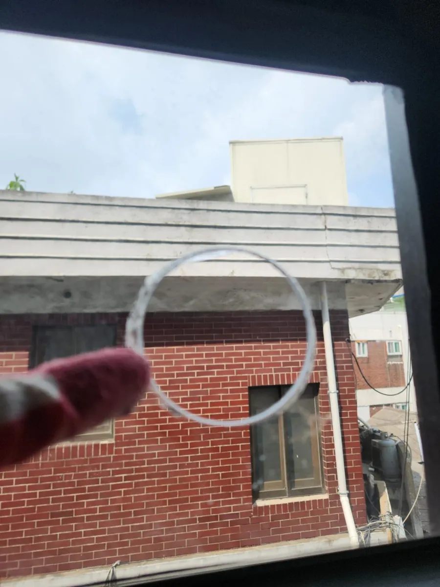 창가에서 원형으로 오려 낸 유리 테두리 너머로 붉은 벽돌 건물이 보이는 장면