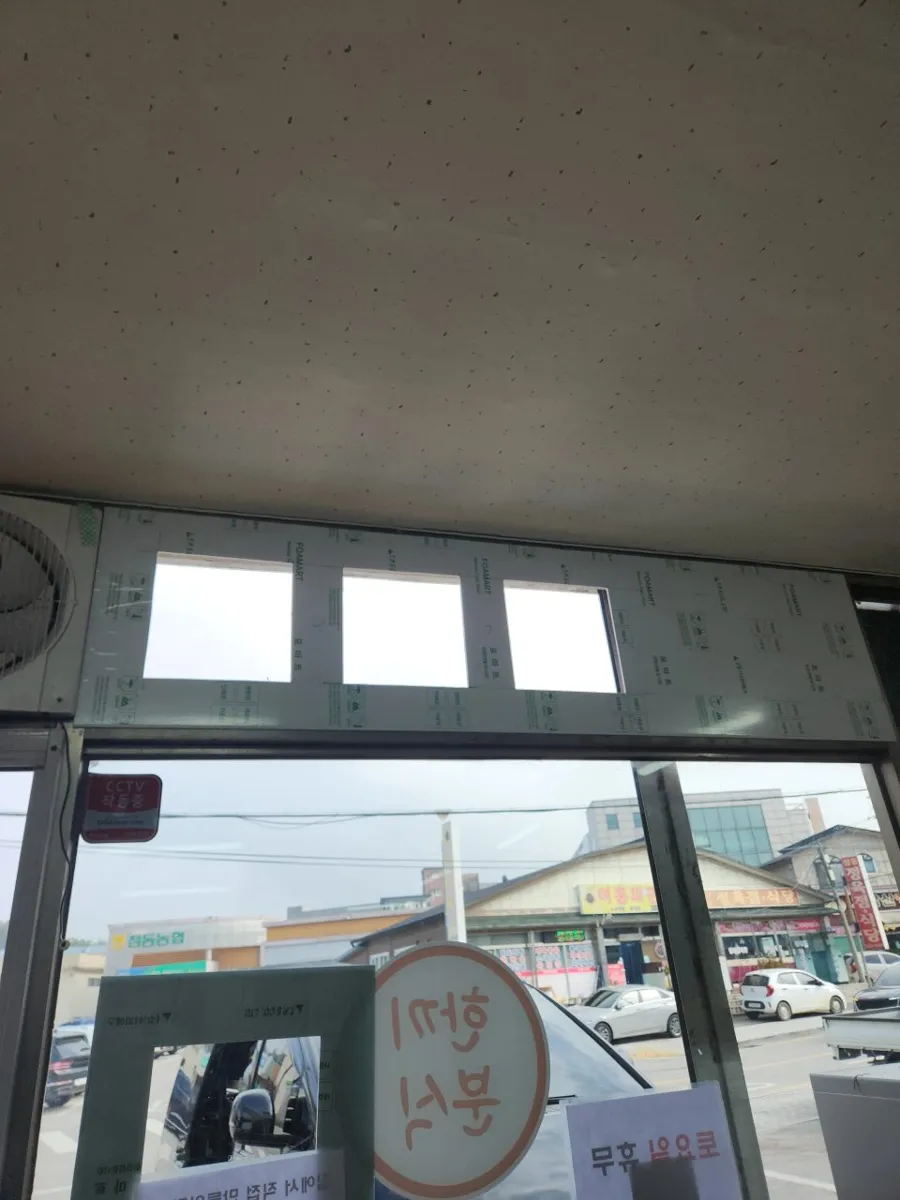 점포 상단 창 틈에 포맘 보드를 대고 사각 구멍 세 개를 낸 환풍기 작업 현장