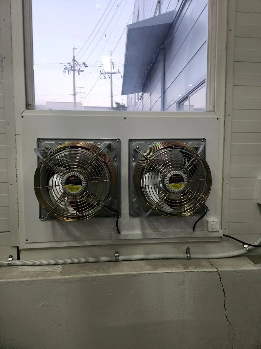 매장 창 안쪽 하얀 판 위에 금속 망 환풍기 두 대가 나란히 설치되고 전선관이 지나가는 모습